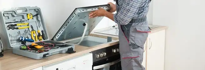 Cooktop repair technician lifting a built-in stovetop for service in Shreveport, LA