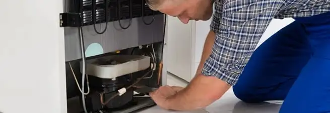 Refrigerator repair technician servicing the compressor and condenser area in Shreveport, LA