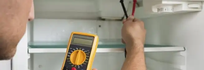 Refrigerator repair technician testing electrical components with a multimeter in Shreveport, LA