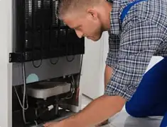 Refrigerator repair technician servicing the compressor and condenser area in Shreveport, LA